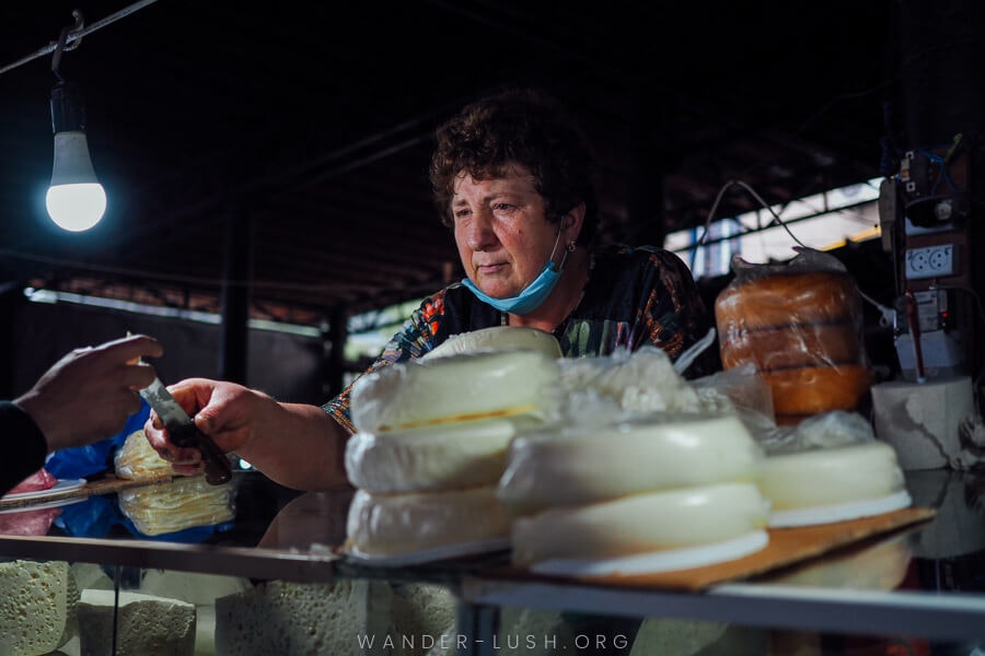 A woman offers up a piece of cheese on the end of a knife.