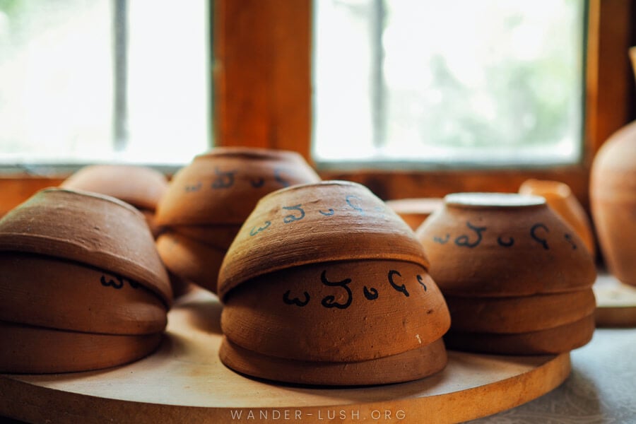 Traditional clay drinking bowls inscribed with Georgian characters stacked on a wooden tray.