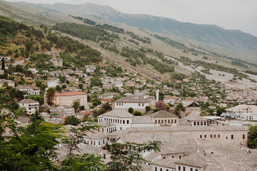 View of the city of Gjirokaster, with stone-roofed houses and green hills.
