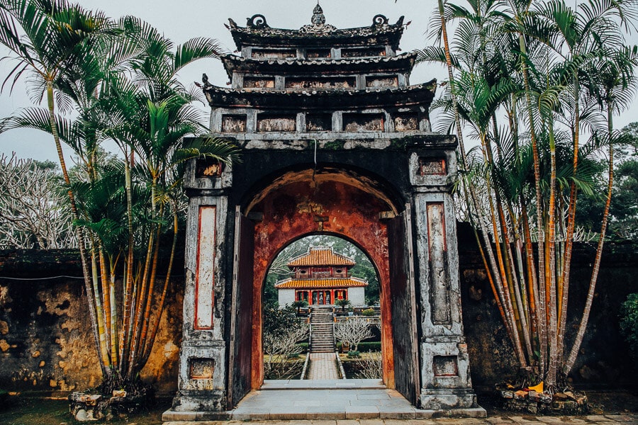 A richly decorated gateway, part of an imperial tomb complex, surrounded by leafy trees.