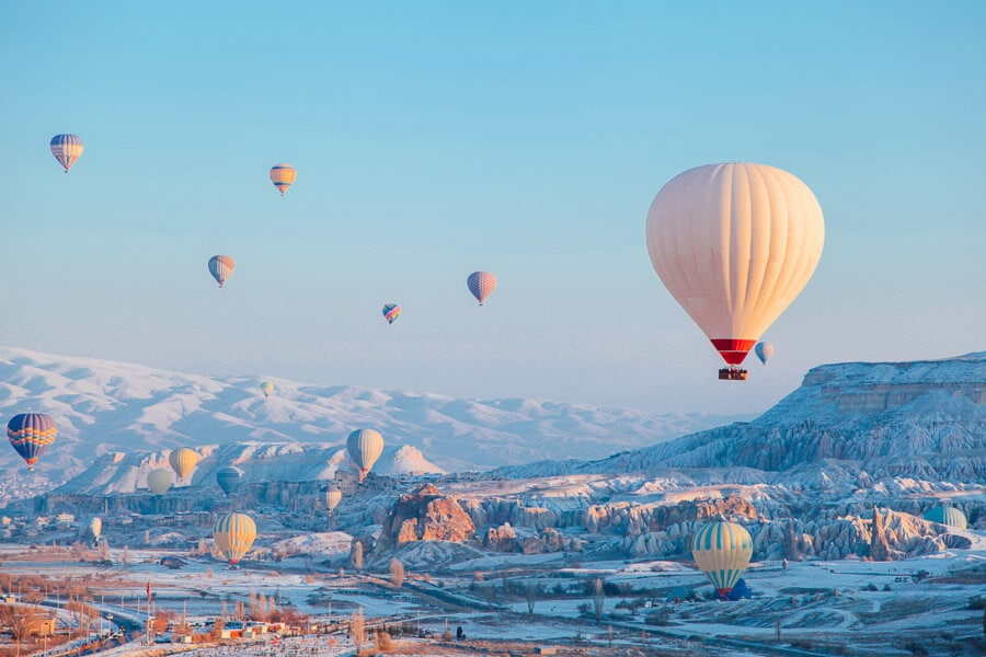 Hot air balloons sail above a snow-covered Cappadocia in Turkey in winter.