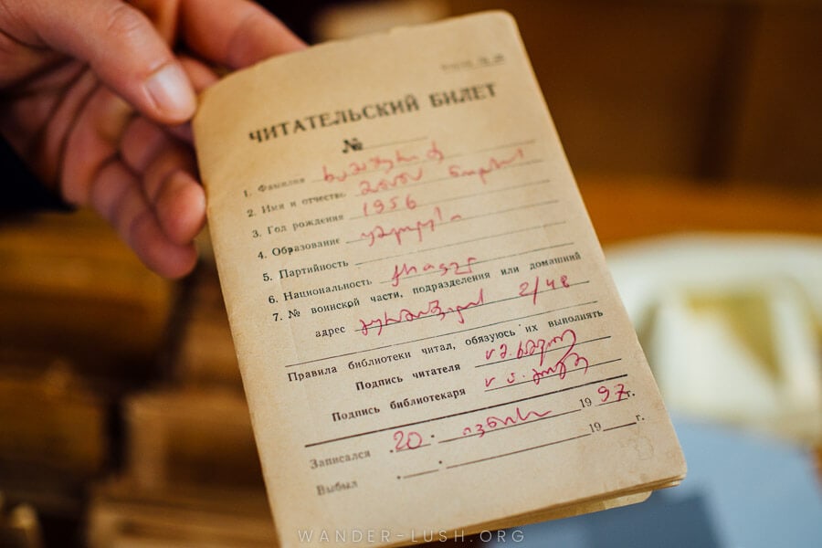 A man holds an old library card with Russian writing.