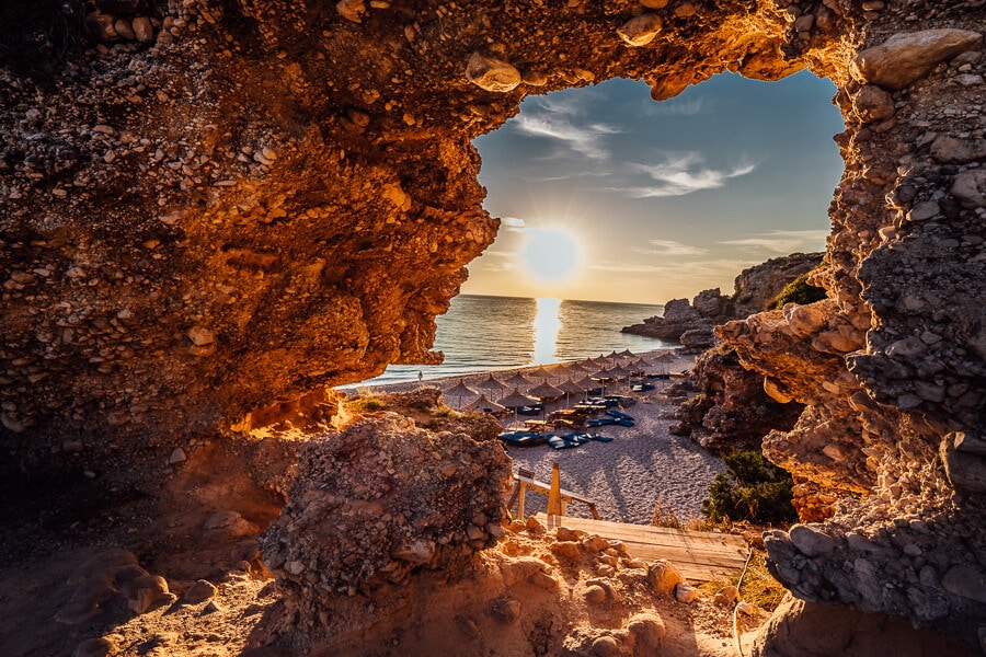 The sun sets through a rock formation on Albania's Dhermi Beach.
