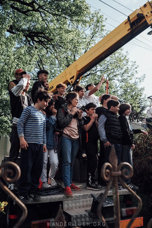 A group of people stand atop a platform in the yard of a house in Shukhuti watching the Lelo Burti festival.