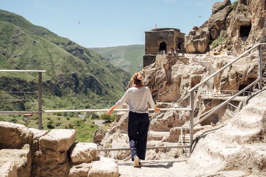 A woman looks out over Vardzia, a complex of caves and tunnels carved from rock above a green valley in Georgia.