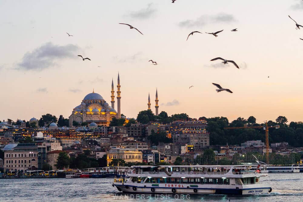 View of Istanbul city at sunset from the Galata Bridge, with a Bosphorus ferry and mosque minarets. Travel tips for visiting Istanbul for the first time.