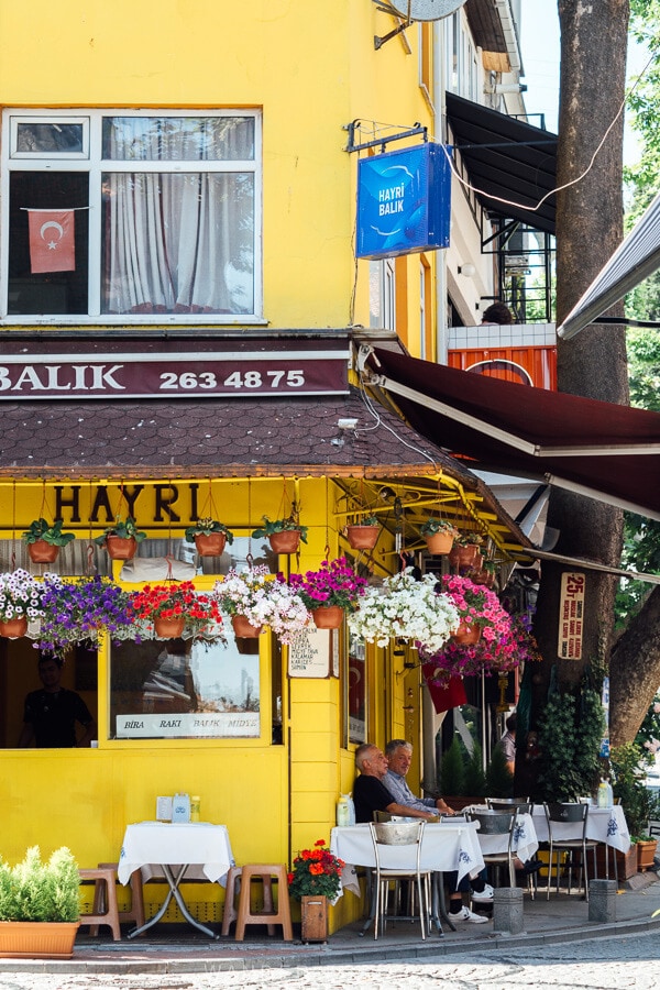 Men sit at a bright yellow restaurant in Arnavutkoy, Istanbul.