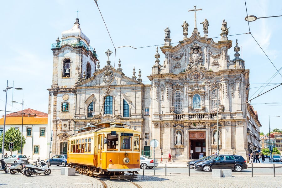 A yellow tram runs past the beautiful Carmo Church in Porto.
