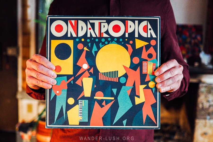 A man holds up a colourful vinyl record of traditional Colombian music.