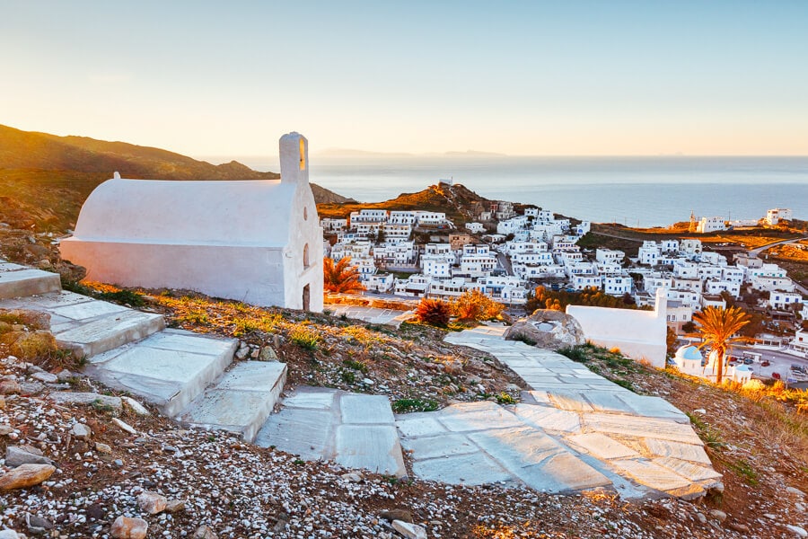 A small church with a winding path overlooks the white architecture of Chora on the beautiful Greek island of Ios.