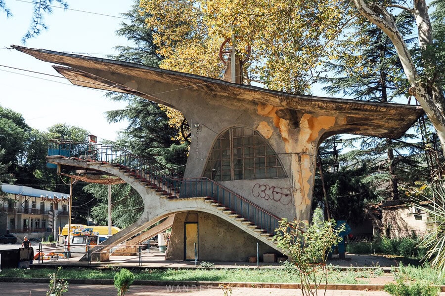 Abandoned Soviet-era cable car station in Chiatura with a sweeping concrete roof and twin staircases, its facade weathered and covered in graffiti.
