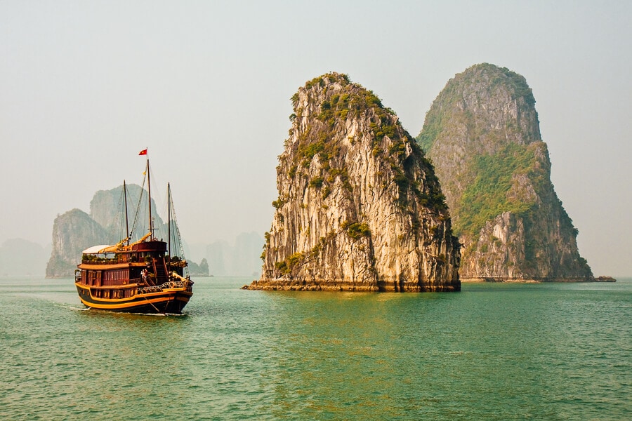 A junk boat sails past two limestone rock formations on Vietnam's Ha Long Bay.