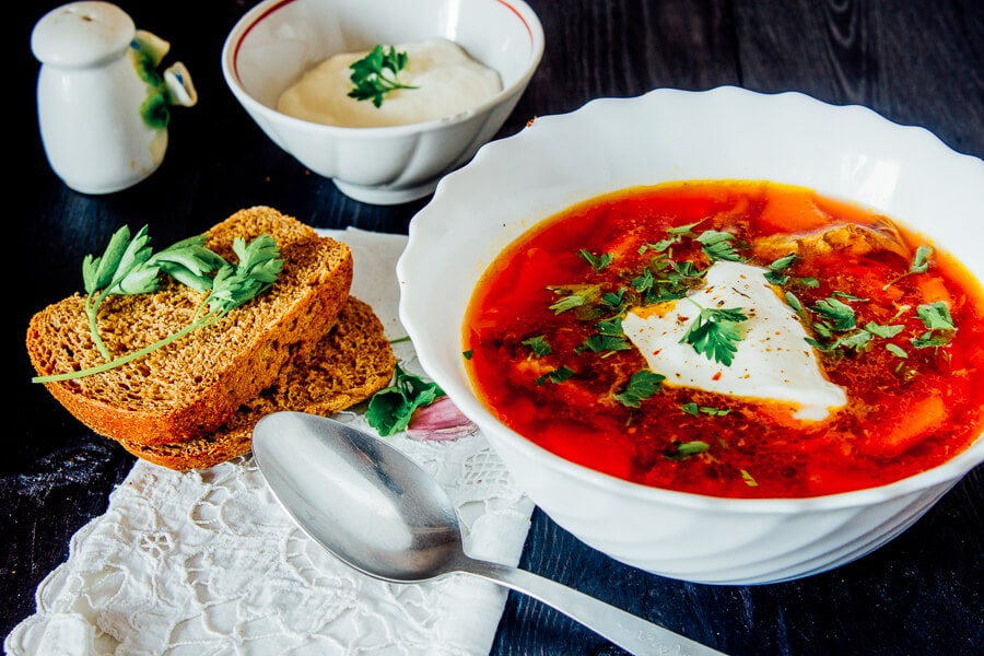 A white bowl of Ukrainian borscht soup with a side of bread and sour cream.