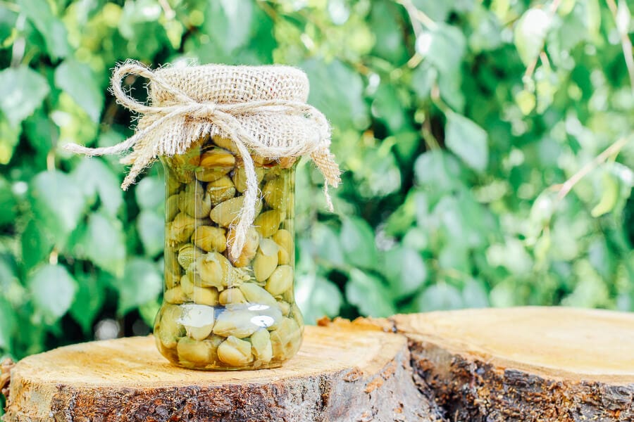 A jar of preserved capers on a wooden log.