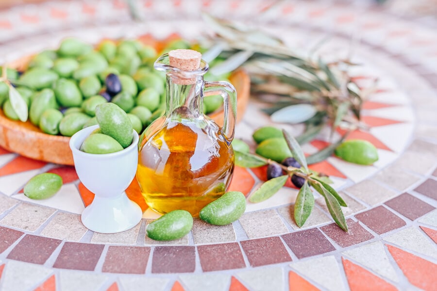 A small decanter of olive oil surrounded by green olives.