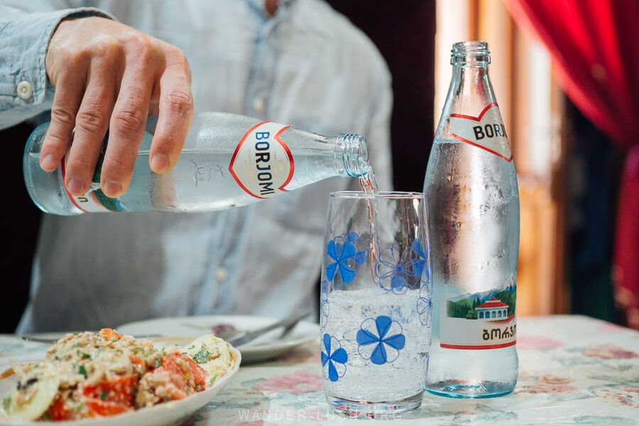 A man pours Borjomi Mineral Water into a tall glass.