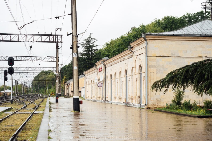 The facade of a historic railway station in Rioni outside Kutaisi, with the tracks running past a yellow stone heritage building.