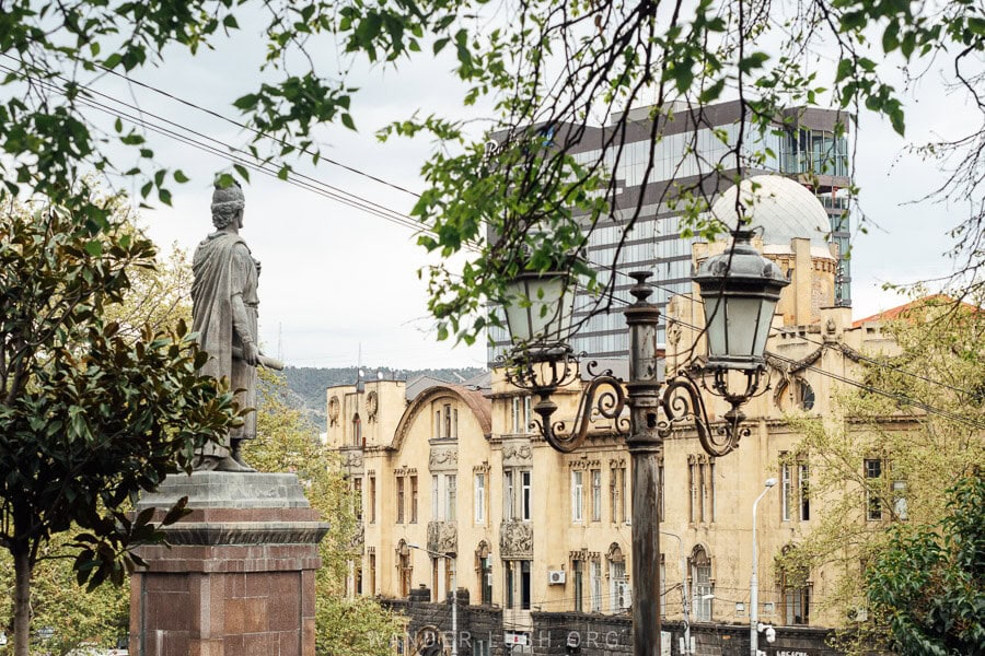 New green spring foliage wraps around a statue of Shota Rustaveli in front of a historic building on Rustaveli Avenue in Tbilisi in April.
