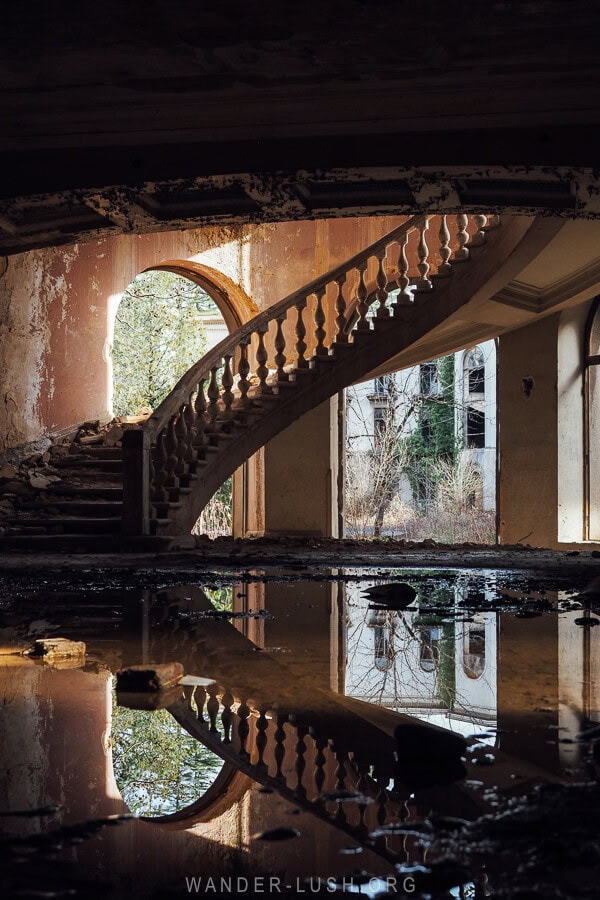 A reflection of a sweeping stone staircase in a puddle inside a beautiful sanatorium in Tskaltubo, Georgia.
