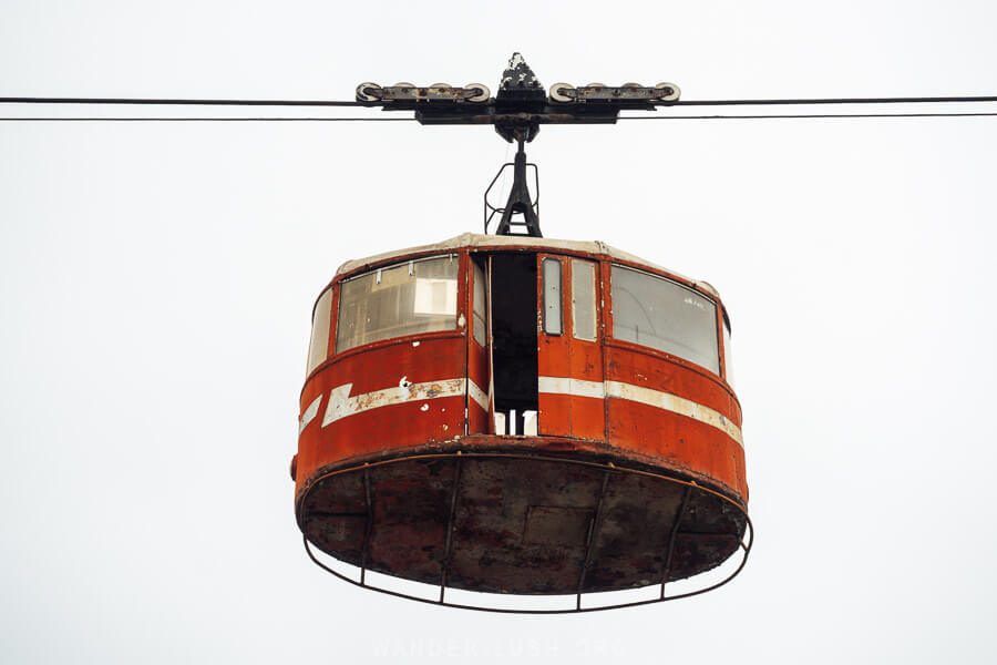 A rusted red gondola hangs from an abandoned cable car line in Tbilisi, Georgia.