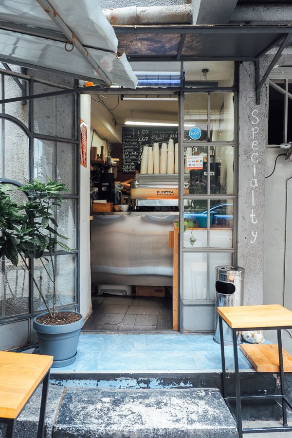 A tiny hole in the wall coffee shop in Tbilisi's Vera district, with a coffee machine and a plant by the door.