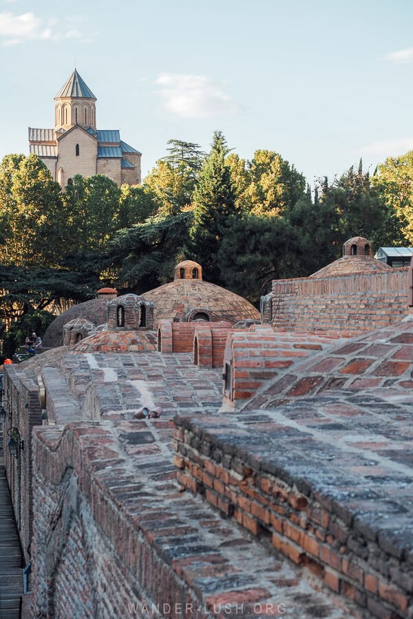 A church stands on a hilltop above the domed brick roofs of the sulfur baths in Tbilisi, an iconic scene from the capital of Georgia.