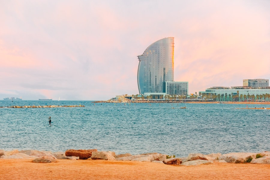 A single paddleboarder on the water at Barceloneta Beach at sunset.