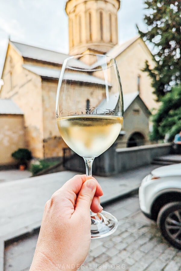 Holding a glass of white wine out in front of Sioni Cathedral in Tbilisi.
