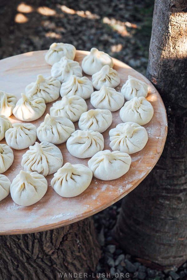 A set of freshly prepared khinkali dumplings sitting on a wooden platter between the trees at a winery in Kakheti, Georgia.