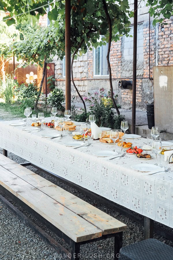 A beautiful long table laid out with a white cloth, plates of Georgian food and wine glasses for a harvest supra in Kakheti, Georgia.