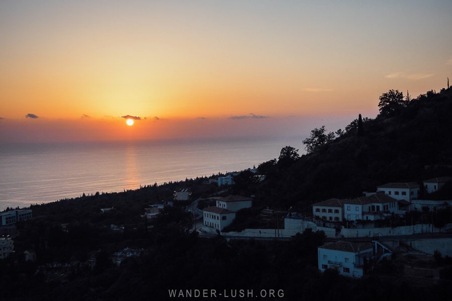 The sun setting over the horizon in Dhermi, with white houses on the hillside.