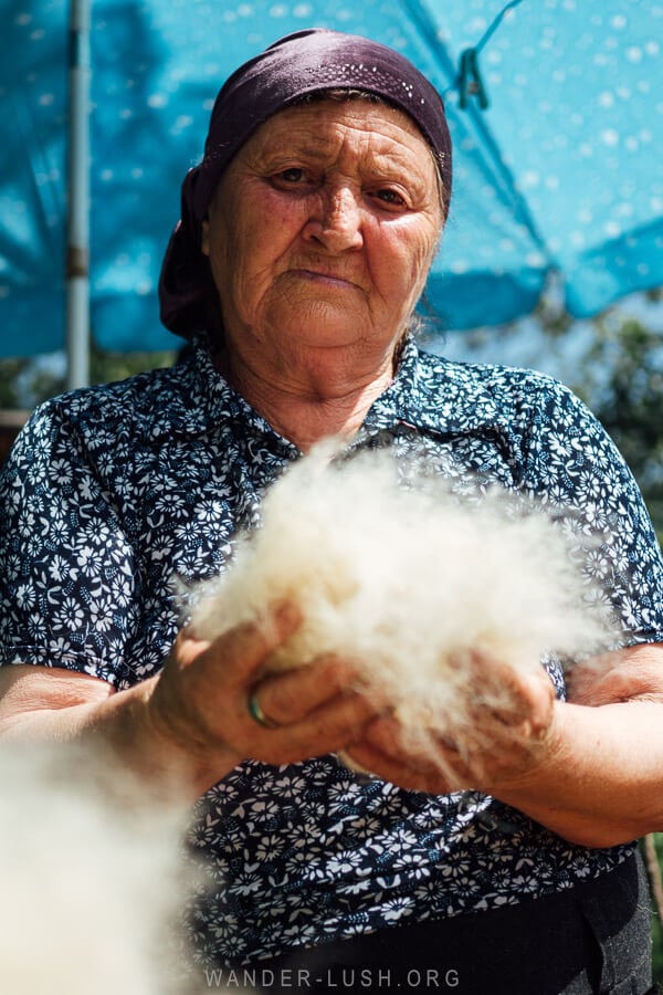 An older woman with a scarf on her head holds a ball of wool felt for the camera, showing her work as a feltmaker in Pankisi Valley, Georgia.