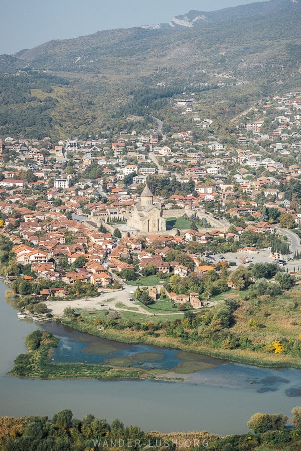 A view of Mtskheta in Georgia, with a large stone cathedral surrounded by red roofs and two rivers meeting.
