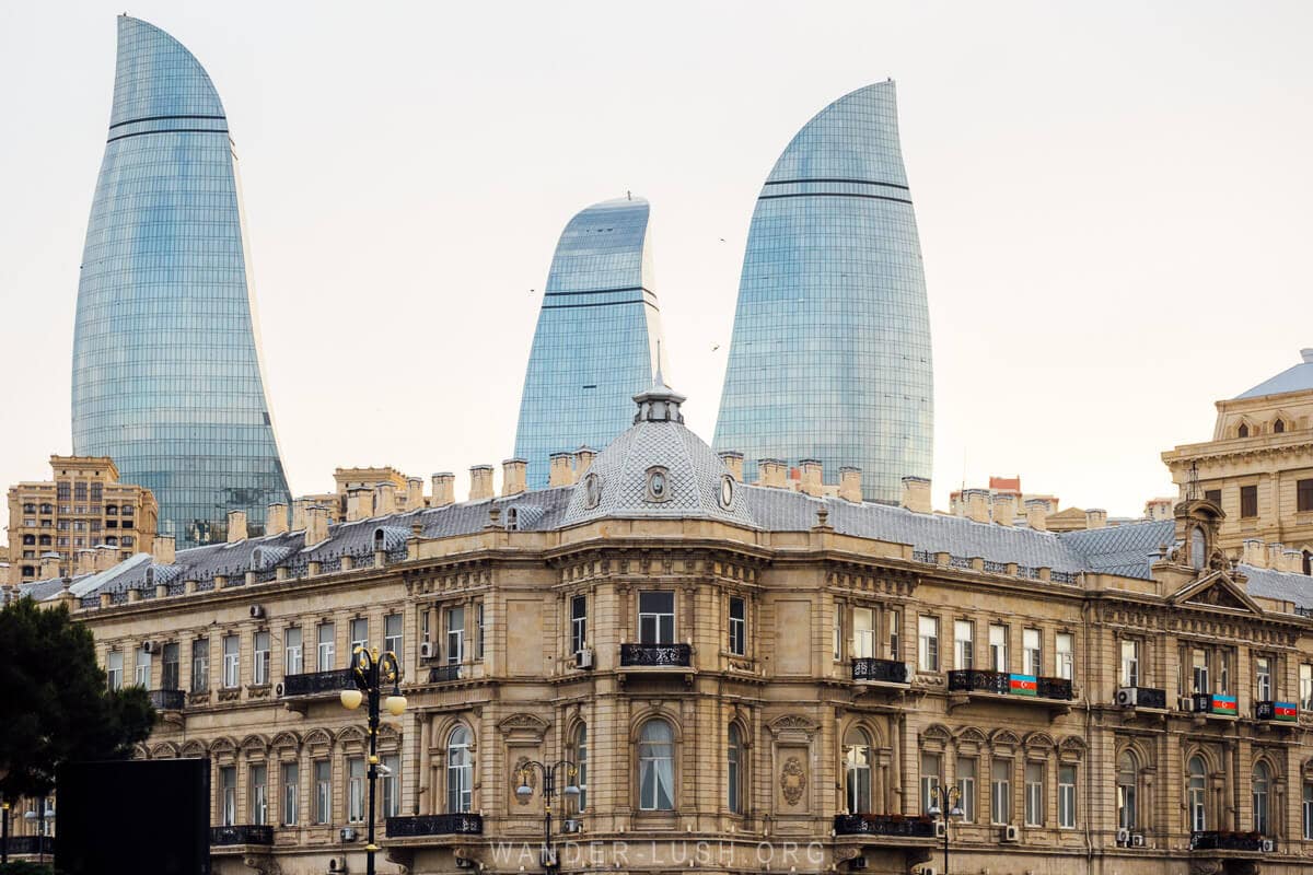 A view of Baku city with a historic 20th-century facade in the foreground and the three modern flame towers rising in the distance.