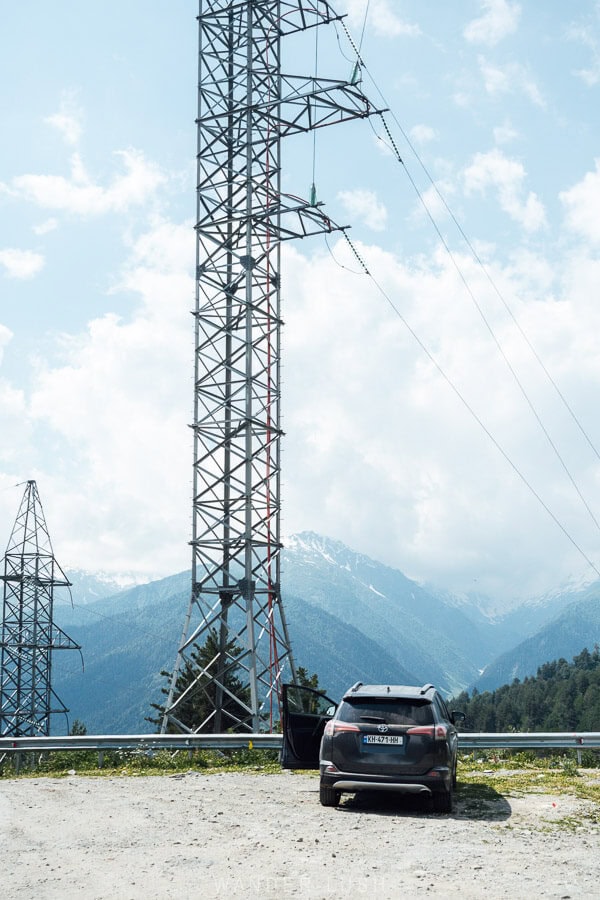 A black car parked beneath a power tower on the Ughviri Pass between Mestia and Ushguli.