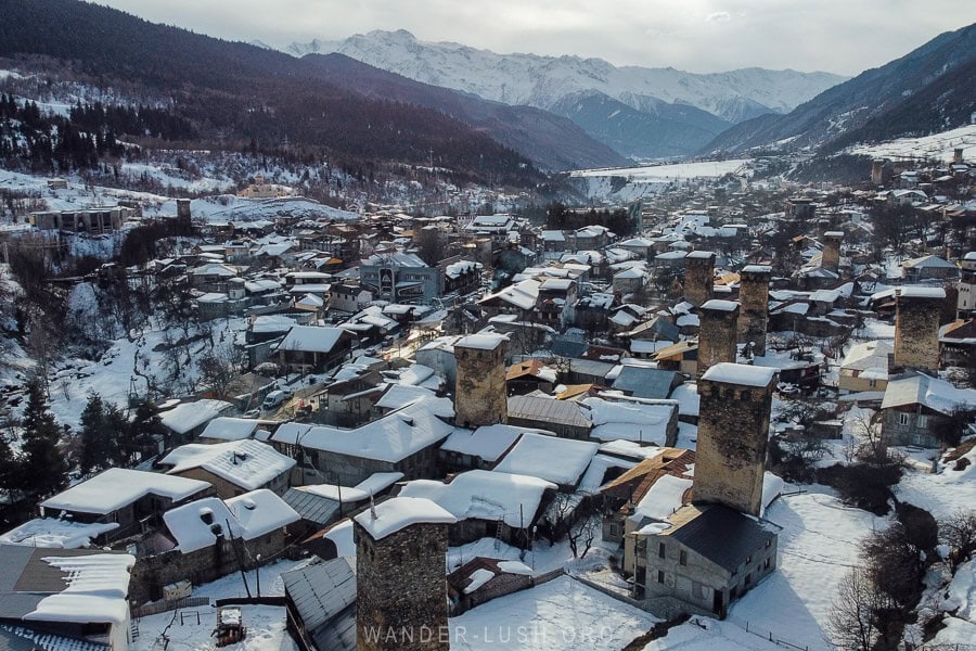 Aerial view of Mestia, Georgia, showcasing its iconic Svan towers and snow-covered rooftops, with the Caucasus Mountains stretching into the distance.