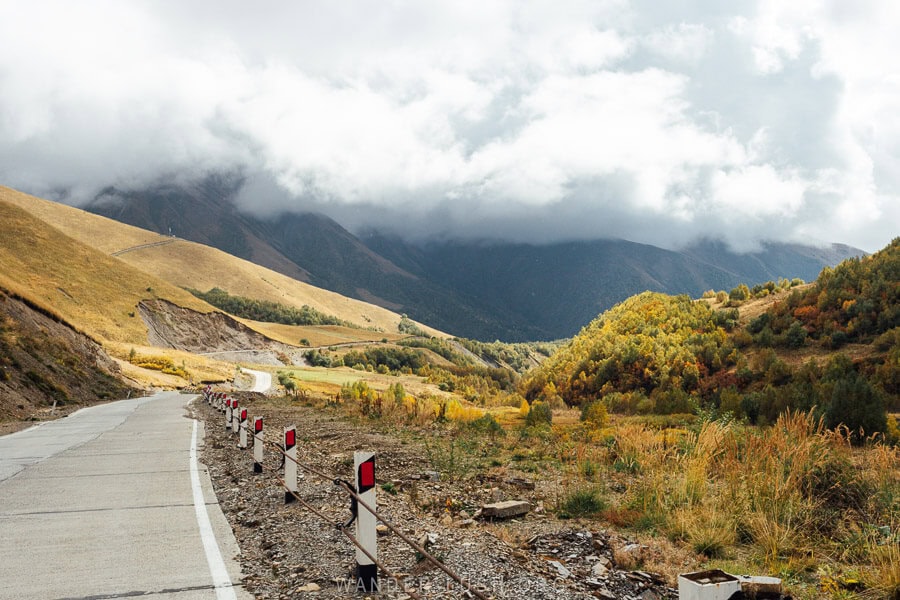 A sealed mountain road winds through yellow and rust-coloured foliage in autumn in Svaneti, Georgia.