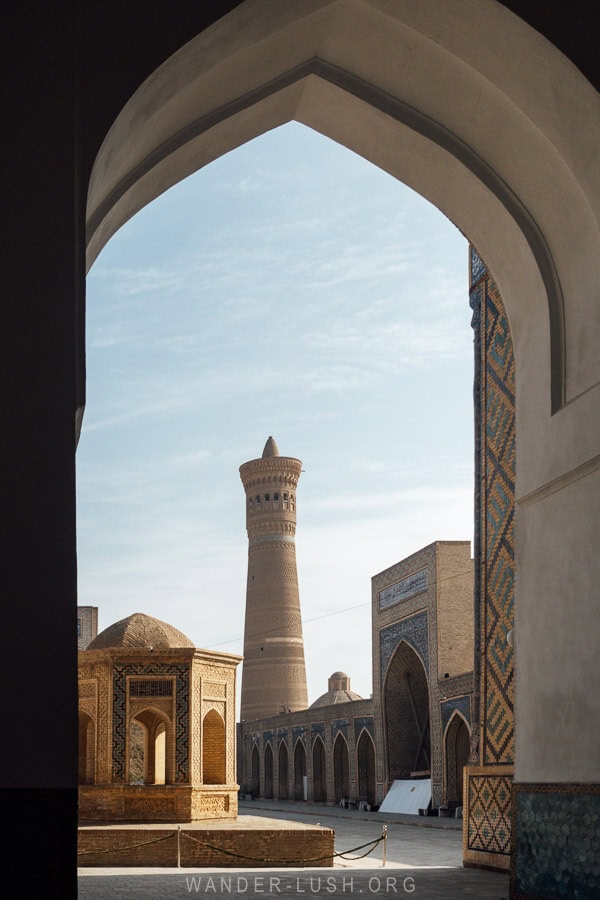 The Kalan Minaret framed by an arched doorway, rising above the surrounding madrasas in Bukhara’s Po-i-Kalyan complex.
