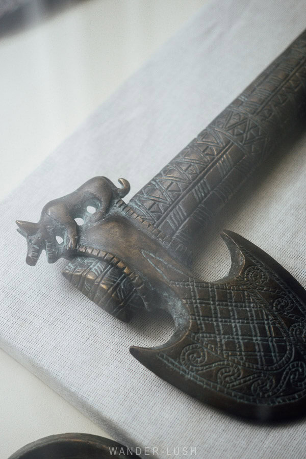 A bronze axe head with detailed carvings and an animal figure inside a glass cabinet at the Kaspi Local History Museum in Georgia.