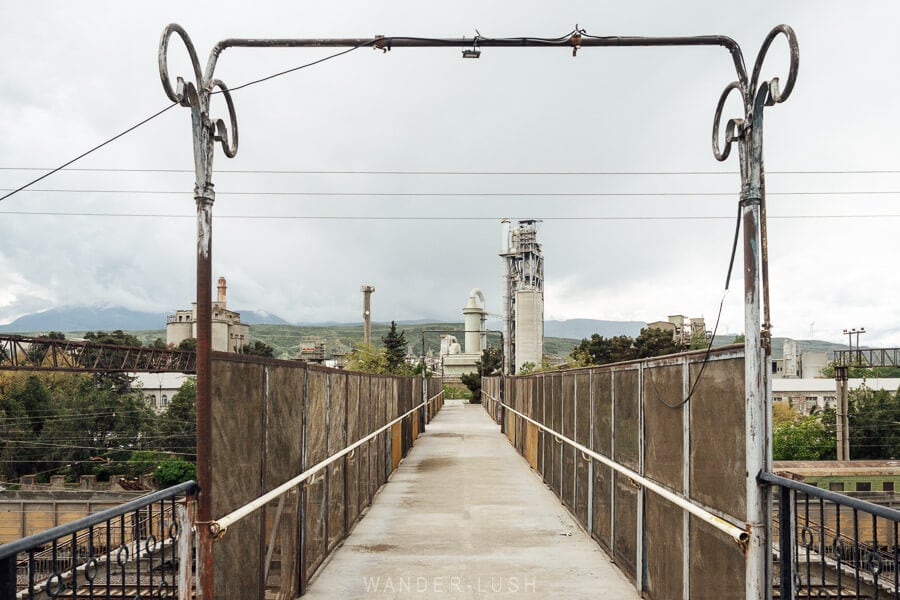 A rusty railway bridge leads towards the Kaspi Cement Factory, a Soviet-era manufacturing facility in Kaspi, Georgia.
