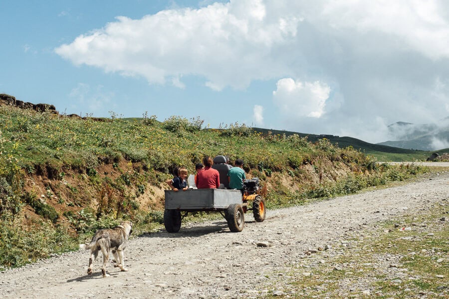 A family riding in the trailer of a tractor with their dog following on the gravel road at the Zekari Pass.