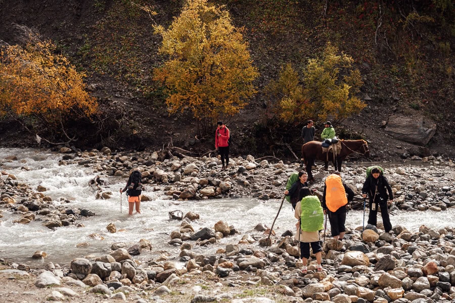 Tourists with colourful backpacks gather on the bank of the Adishchala River in Svaneti, preparing to cross the river on the way to Ushguli.