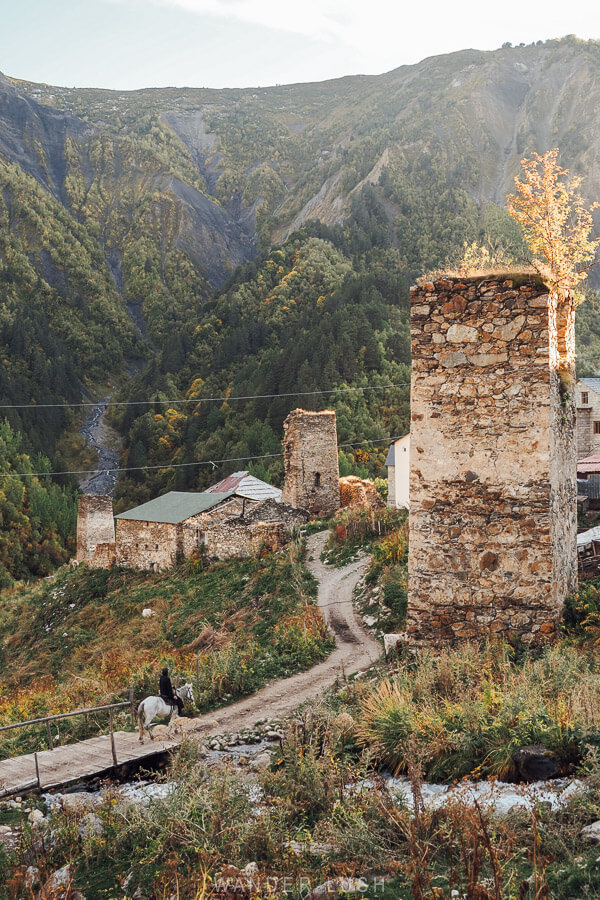 A man rides a white horse over a bridge crossing a steam in the village of Adishi, Georgia.