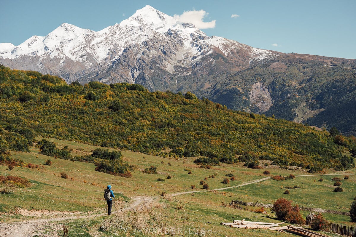 A man moves across a narrow track beneath a snow-capped mountain in Svaneti on day two of the hike from Mestia to Ushguli in Georgia.
