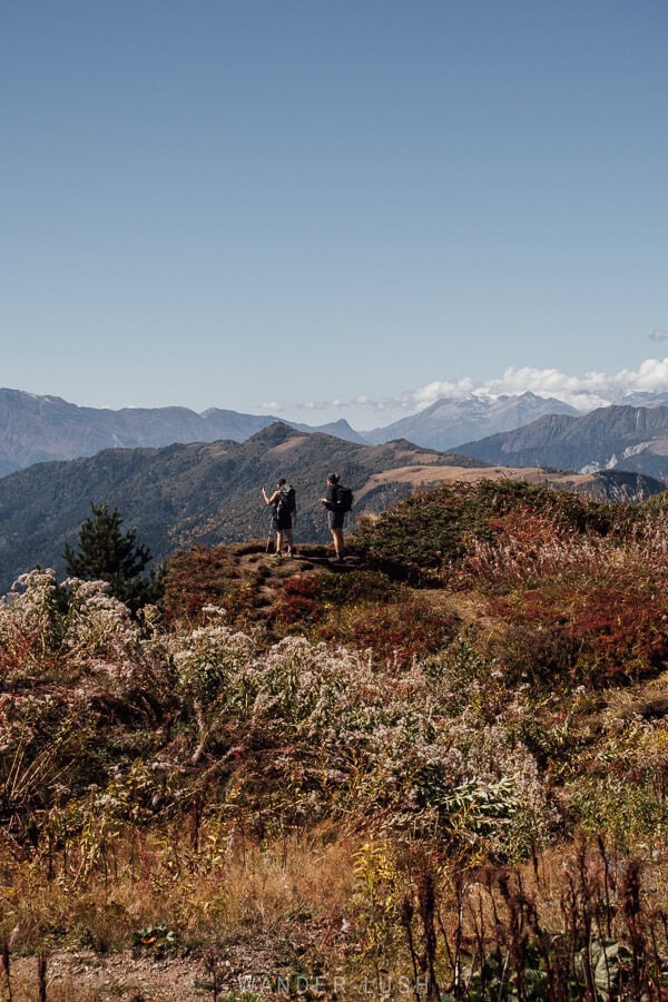 Two people look out over a sea of mountains amidst autumn foliage on the hike from Mestia to Ushguli.