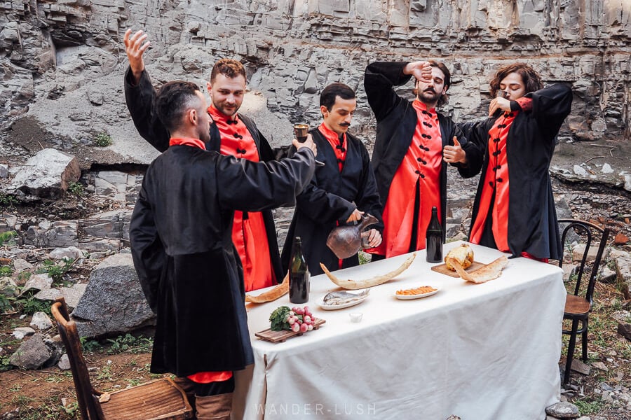 Five men dressed in Old Tbilisi costume act out a supra, raising wine glasses and kantsi horns in a toast.