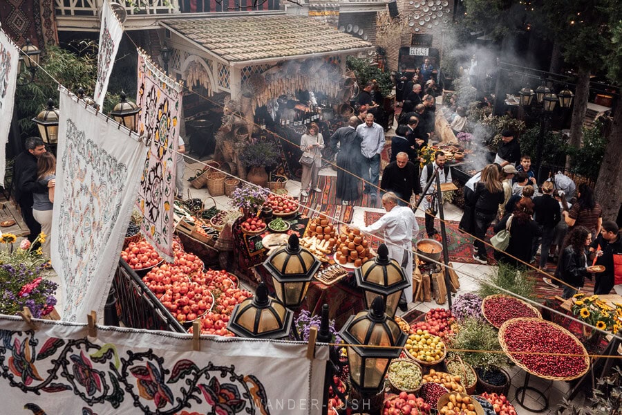 A huge display of produce and flowers, with smoke rising from grills and people gathering around in the courtyard at Georgian House restaurant during the Tbilisoba festival.