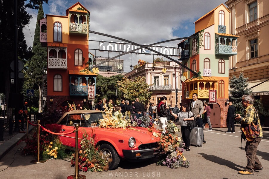 People photograph a flower display atop a vintage car at the entrance to the Tbilisoba festival on Orbeliani Square.