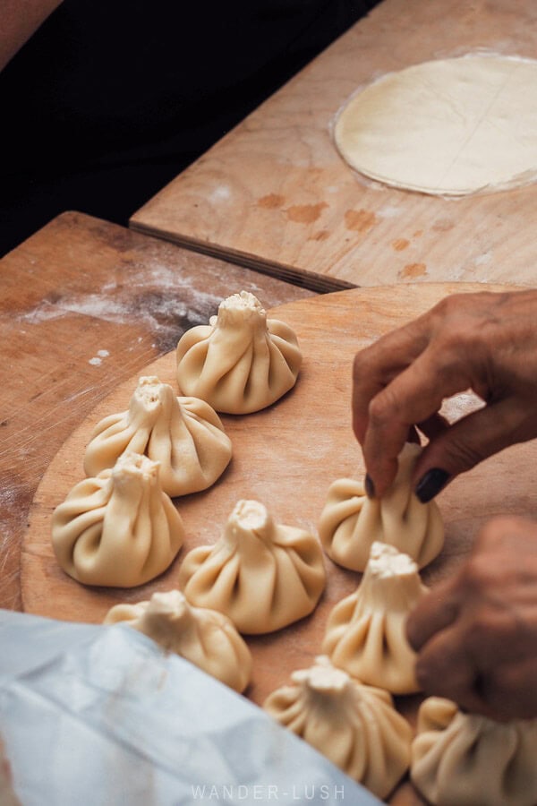 A woman makes khinkali dumplings and lays them on a wooden board.