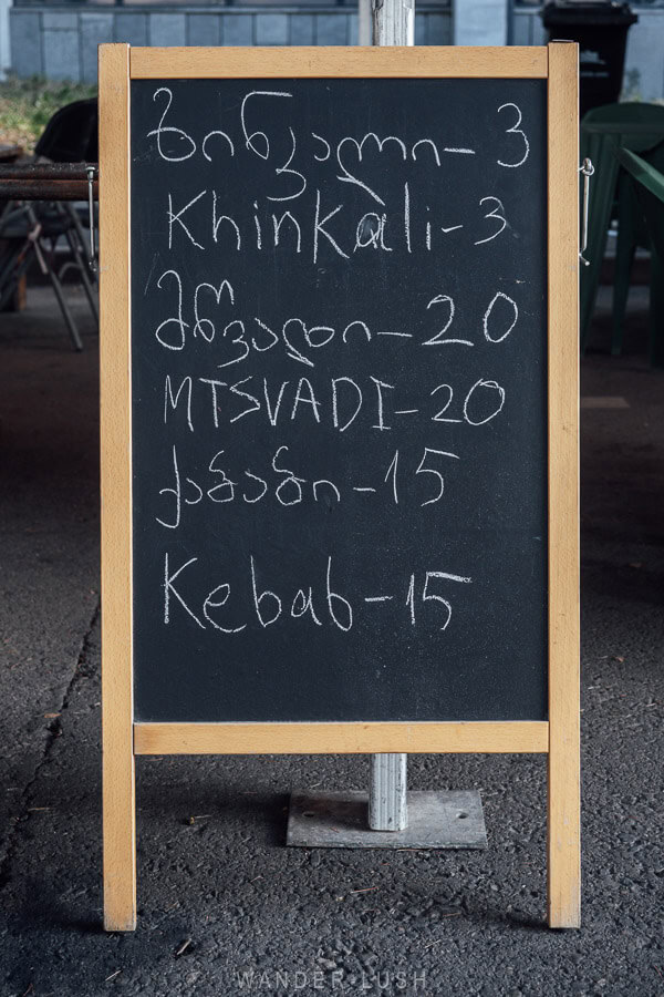 An a-frame blackboard with a menu of Georgian dishes at a street food market in Tbilisi.